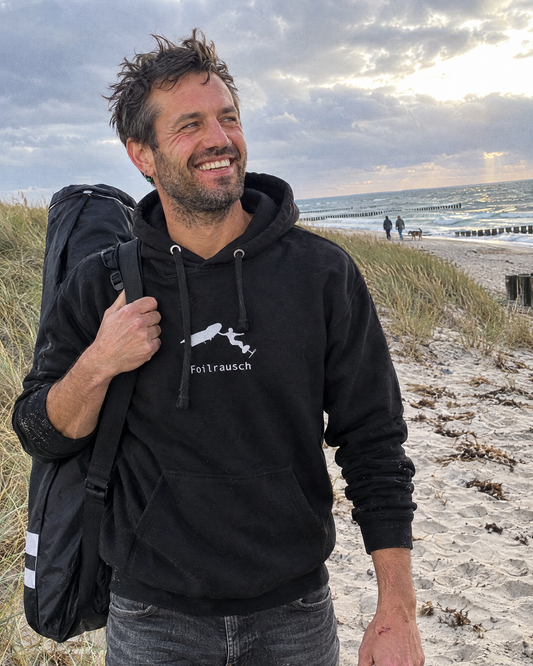 Foilrausch Hoodie in Schwarz getragen am Ostseestrand nach dem Wingfoilen