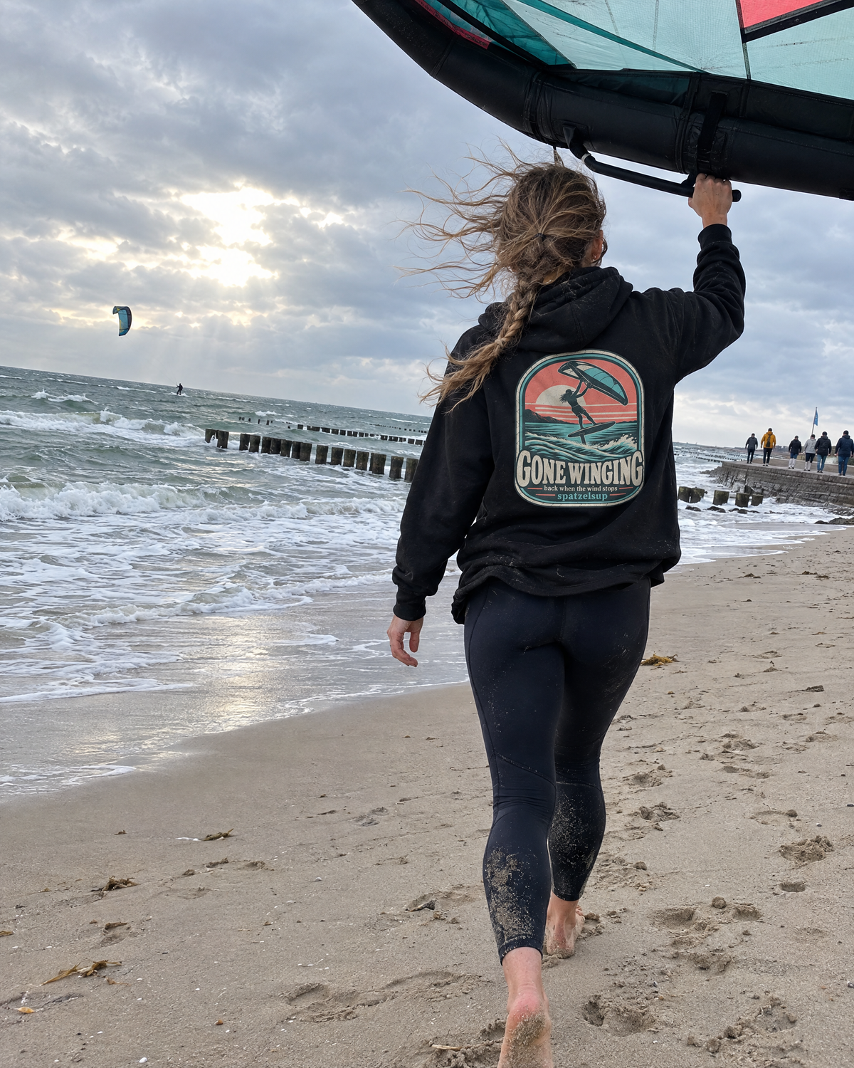 Wingfoilerin im schwarzen Gone Winging Hoodie mit Wing am Ostseestrand