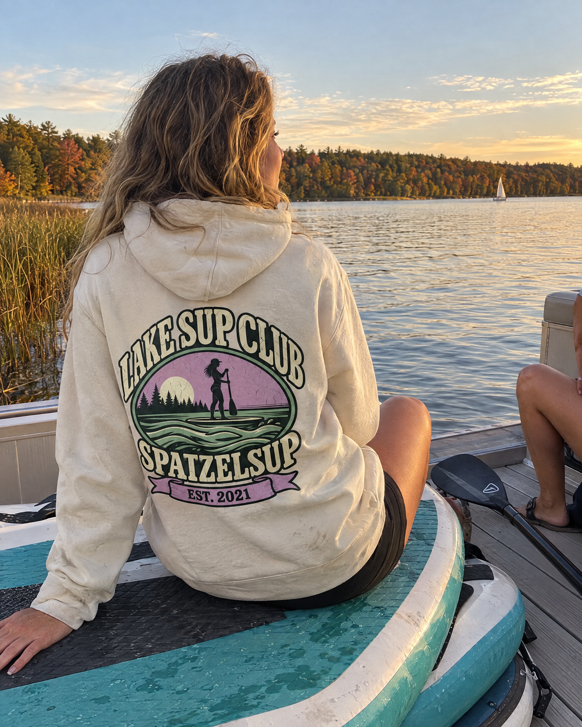 Frau im Lake SUP Club Hoodie in Bone sitzt auf SUP-Boards am Ponton