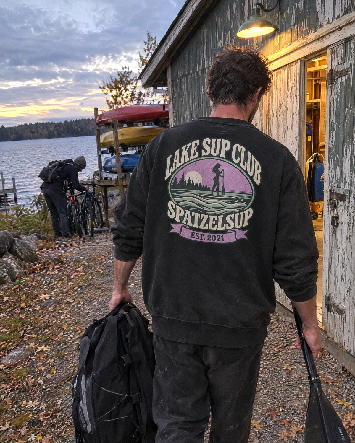 Mann im Lake SUP Club Oversized Pullover vor dem Bootshaus, Rückenprint sichtbar